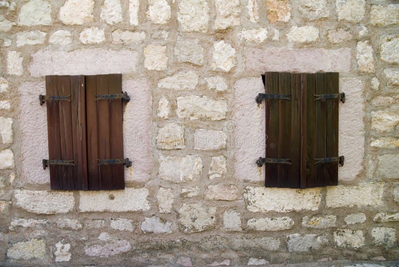 A closeup of two wooden windows on an old stone wall of a building. A closeup of two wooden windows on an old stone wall of a building.