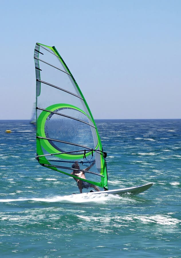 Experienced windsurfer speeding along with a green sail on a sunny blue sea giving a real feeling of motion. Experienced windsurfer speeding along with a green sail on a sunny blue sea giving a real feeling of motion.