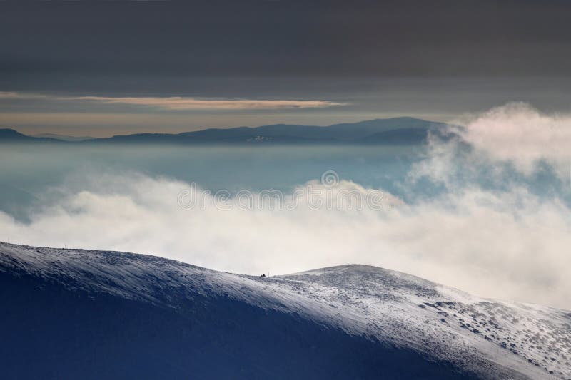 Veterné snehové pole nad oblakmi a hmla za úsvitu Slovenské Karpaty