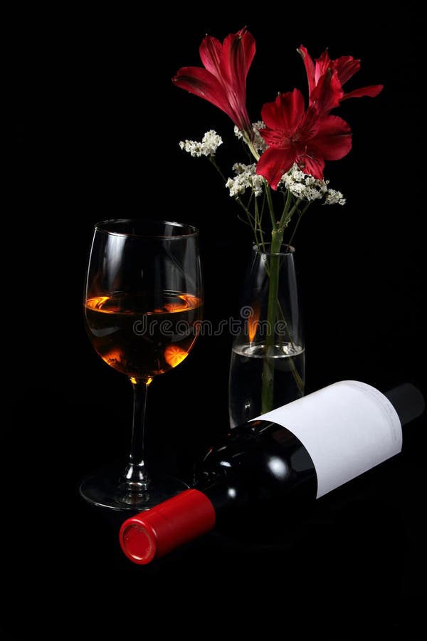 Image of glass of wine and an unopened bottle of wine with flowers, on black background. Image of glass of wine and an unopened bottle of wine with flowers, on black background.