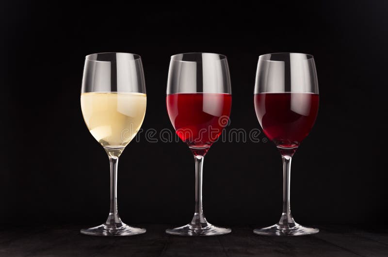 Wine glasses set with red, rose, white wine, mock up on elegant dark black wooden background.