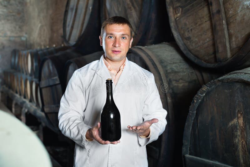 Wine House Technician Holding Bottle Near Wooden Barrels Stock Image