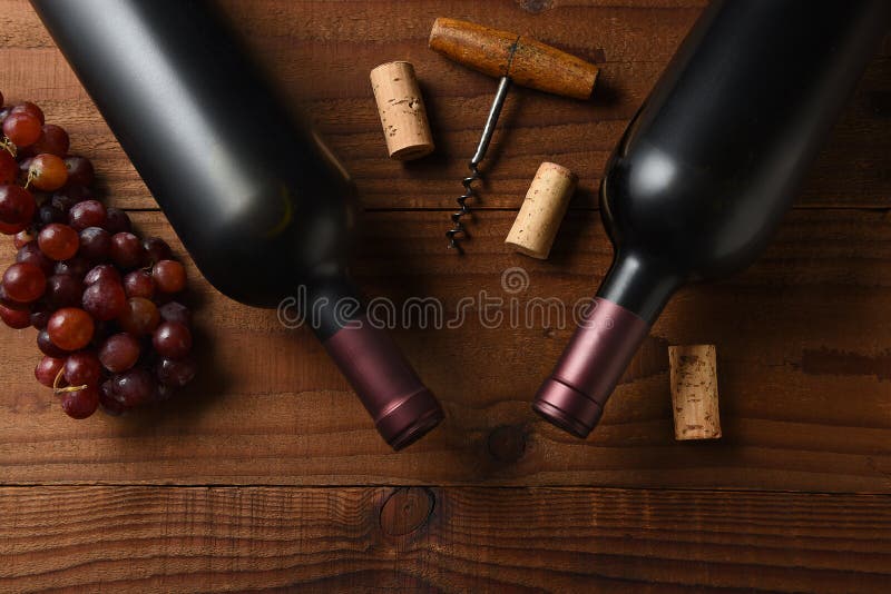 Two Cabernet Sauvignon wine bottle short from directly above on a dark wood table with grapes corks and cork screw and copy space