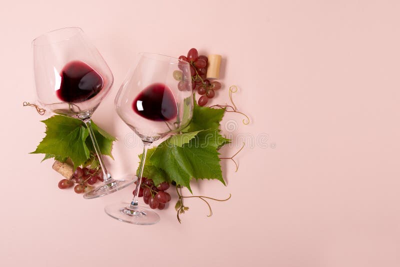 Wineglasses z czerwonym winem, winogronem, liśćmi i korkowym lying on the beach na różowym tle, Wina degustation poj?cie Mieszkan fotografia stock Wineglasses z czerwonym winem, winogronem, liśćmi i korkowym lying on the beach na różowym tle, Wina degustation poj?cie Mieszkan fotografia stock