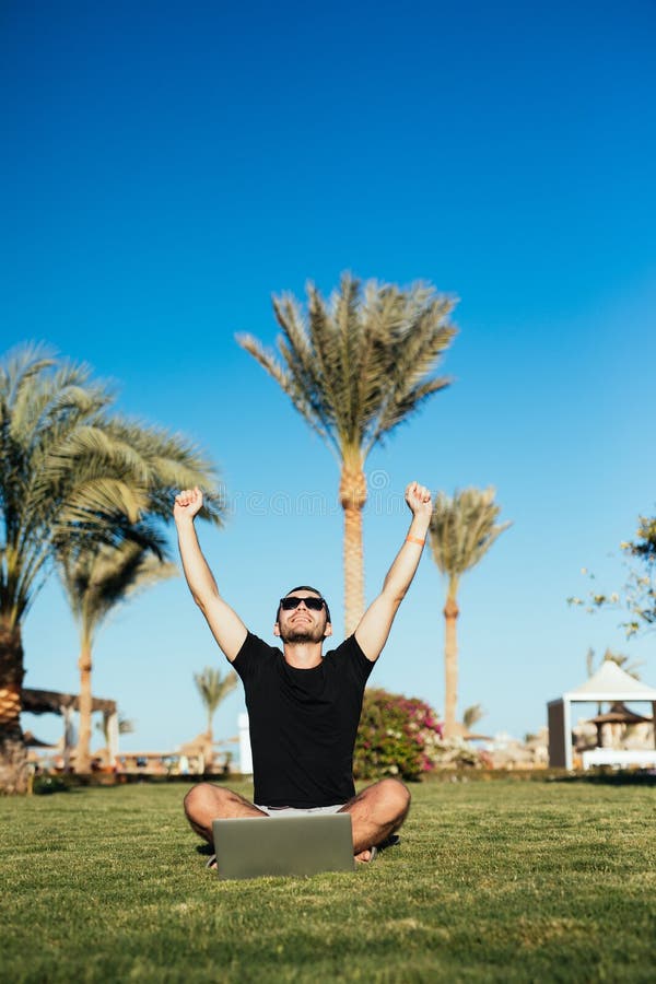Winner. Handsome Man Sitting on the Grass and Use Laptop with Victory
