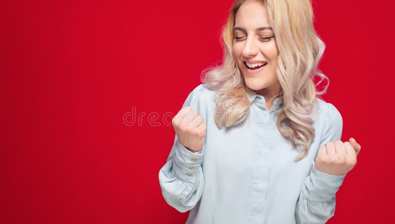 Winner woman with clenched fist celebrating her success, isolated on red background. Cheerful girl