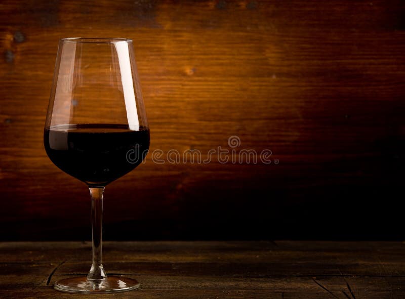 Photo of delicious dark red wine goblet on wooden table illuminated by spot. Photo of delicious dark red wine goblet on wooden table illuminated by spot