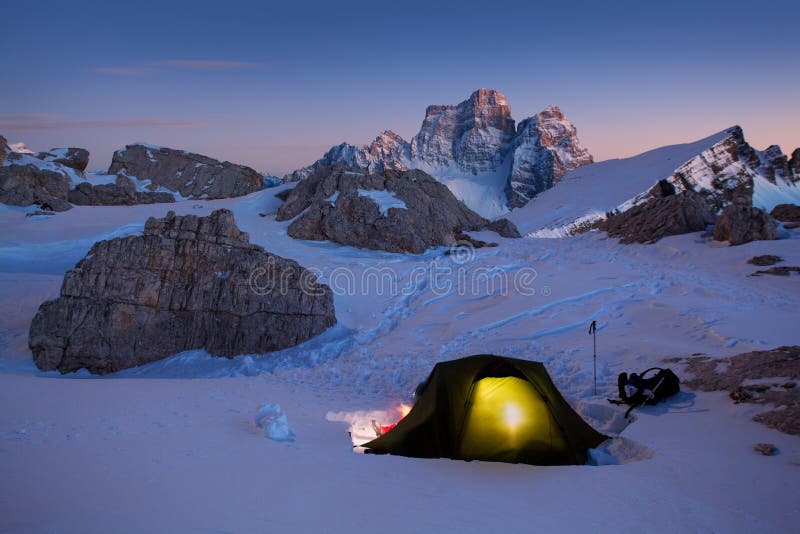 Winter camping, night, shining green tent on snow. Night shot, long exposure, sleeping on snow in the outdoors. Alps Mountains landscape panoramic view. Gorgeous winter day in Dolomites, Italy. Christmas time. Happy new year.