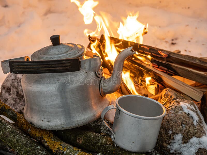Metal tea kettle heating up over a campfire stock photo - OFFSET