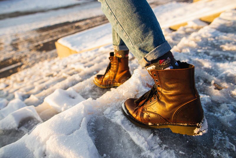 Winter is coming. Female boots on rough slipper ice surface. A woman in brown leather shoes descends the slippery ice