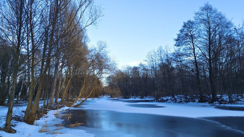 In winter everything is covered with snow and the river is covered with ice. There are footprints in the snow. There is a park of royalty free stock photo