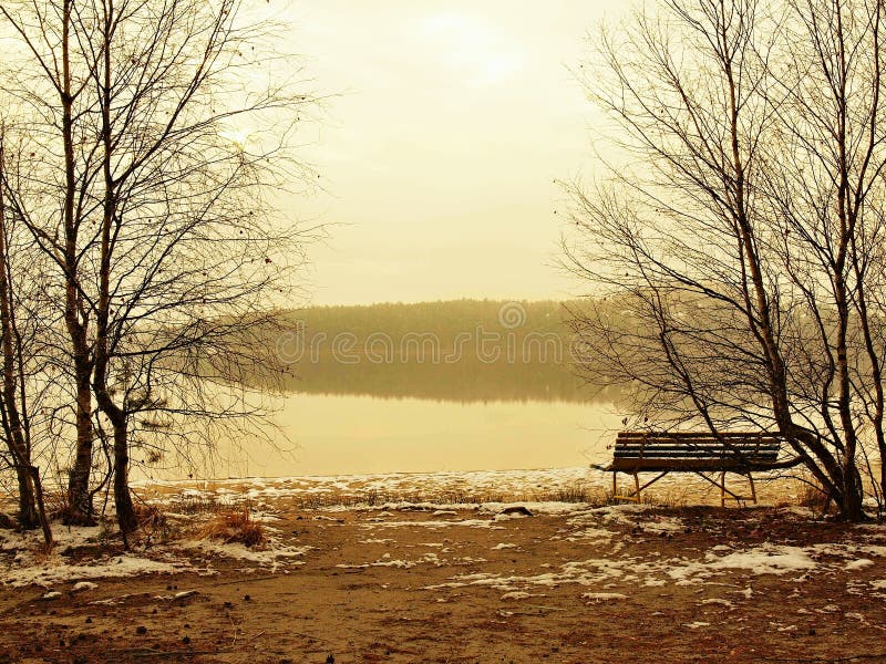 Winter Fogysonnenuntergang über See, kalte orange Sonne strahlt zwischen Überwasserniveau aus. Geschmolzener erster Schnee aus den lizenzfreies stockbild Winter Fogysonnenuntergang über See, kalte orange Sonne strahlt zwischen Überwasserniveau aus. Geschmolzener erster Schnee aus den lizenzfreies stockbild