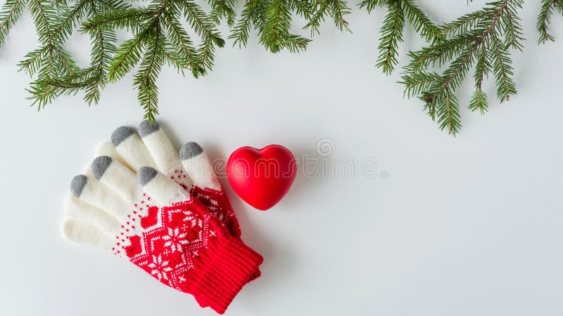 Winter gloves with big red heart in spruce branches on a white table. Christmas and New Year concept. Flat lay, top view.