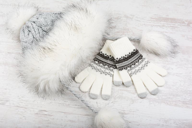 Winter hat with fur and knitted gloves on white wooden background