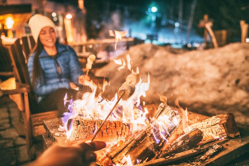 Winter holiday ski resort woman roasting marshmallows in BBQ firepit afterski fun leisure activity with friends. Couple