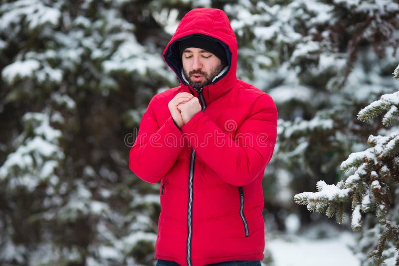 Winter male portrait. Young bearded man trying to heat his cold hands in frost winter park. Cold season concept