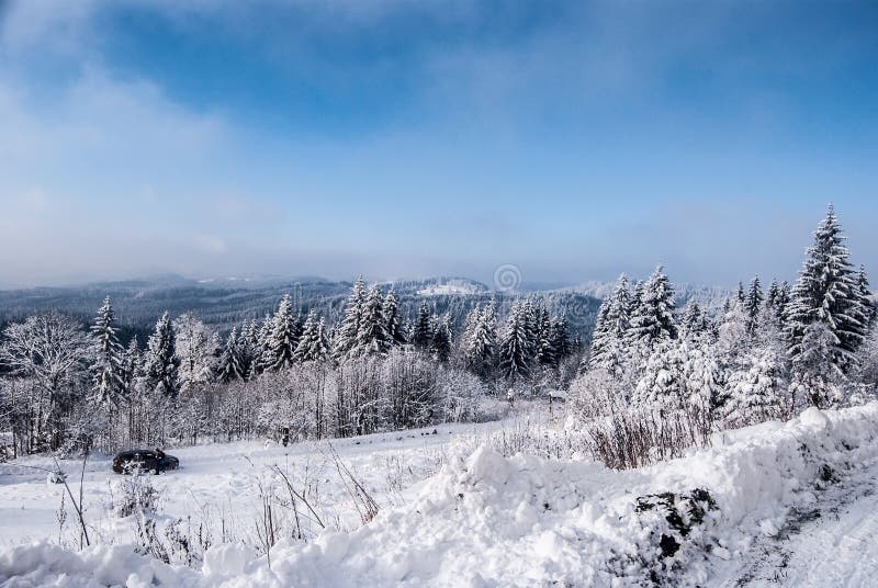 Winter mountain landscape with snow covered road, forest, hills, snow and blue sky with clouds