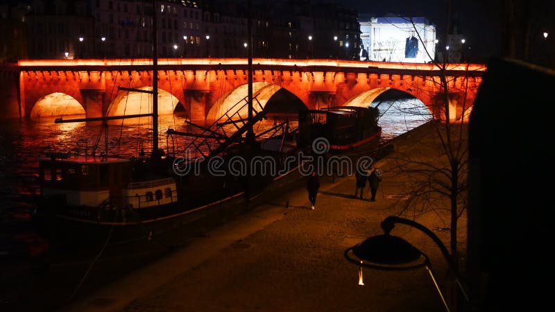 Winter Night Traffic de-a lungul Senei cu o barcă andocată și un pod istoric iluminate în Orange royalty free stock images