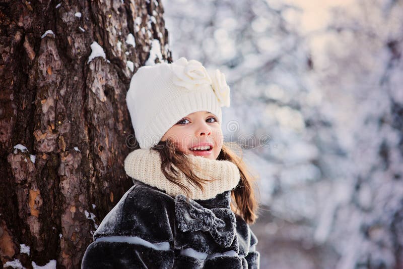 Winter portrait of beautiful smiling child girl standing by the tree