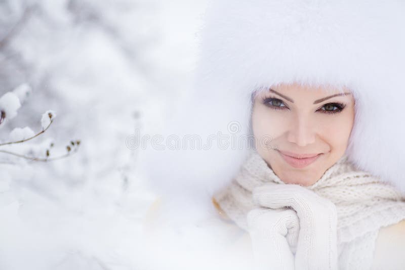 Winter portrait of beautiful smiling woman with snowflakes in white furs