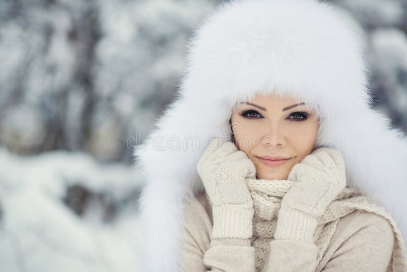 Winter portrait of beautiful smiling woman with snowflakes in white furs