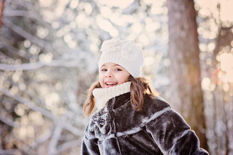 Winter portrait of cute smiling child girl on the walk in sunny snowy forest