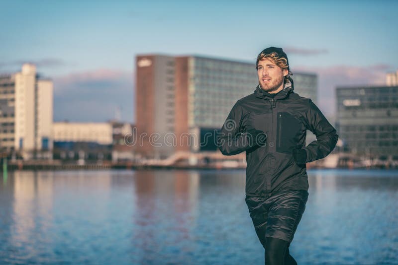 Winter run man jogging outdoor in city harbour running outside wearing cold weather accessories - hat ,gloves