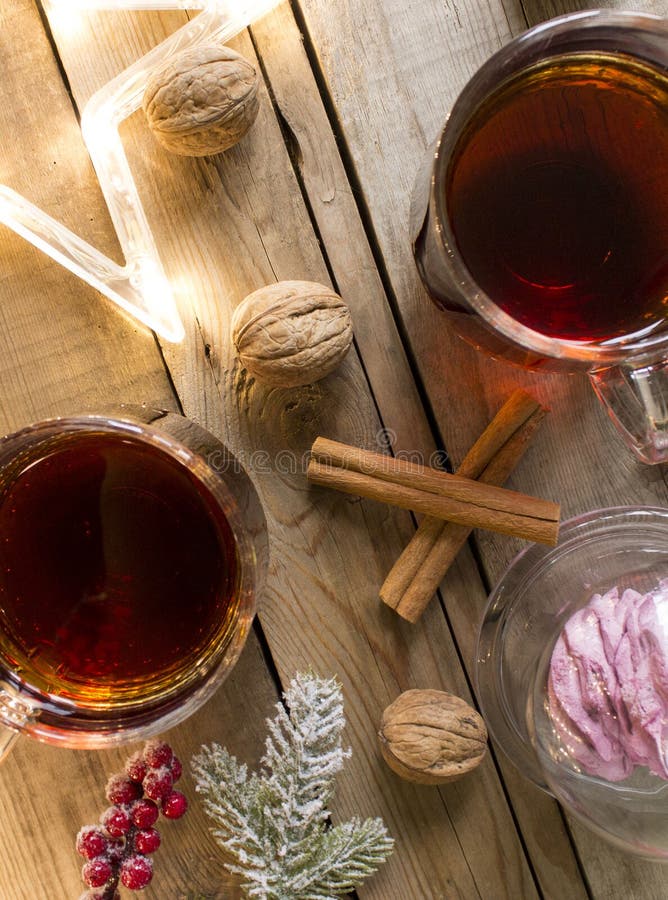 Winter tea party with dessert in a glass capsule on a wooden table. Christmas lights garland of stars, walnuts and cinnamon sticks