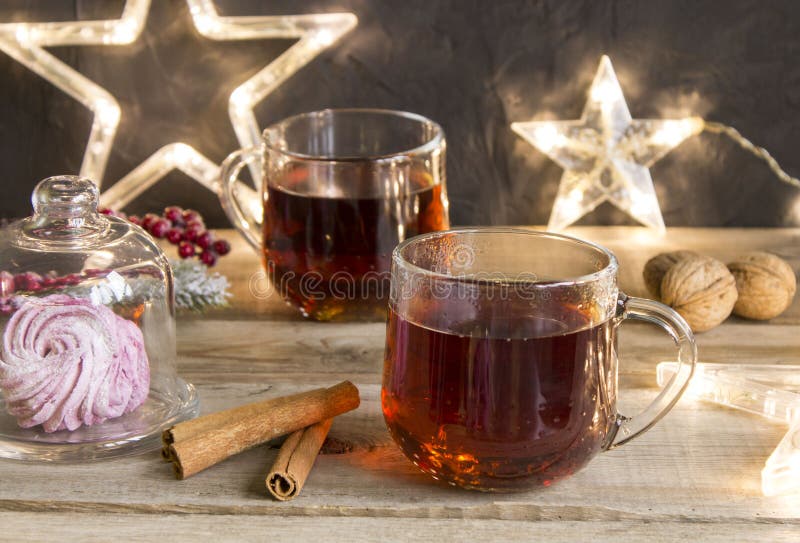 Winter tea party with dessert in a glass capsule on a wooden table. Christmas lights garland of stars, walnuts and cinnamon sticks