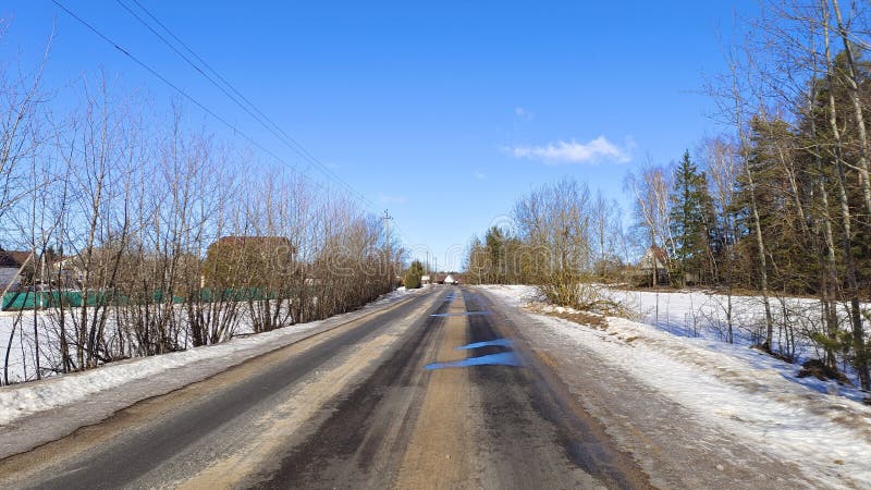 In winter, there is snow on the fields. Under the rays of the bright sun, the snow melts on the asphalt road. Along the road are h royalty free stock photography