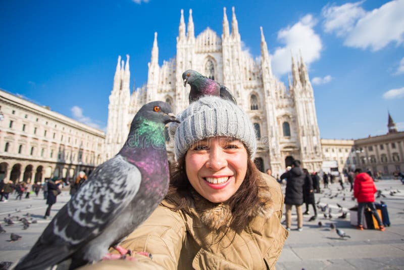 Winter travel, vacations and birds concept - Young funny woman taking selfie with pigeons near Milan Cathedral Duomo di