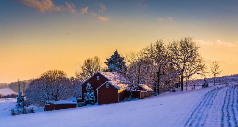 Winter view of a barn on a snow covered farm field at sunset, in