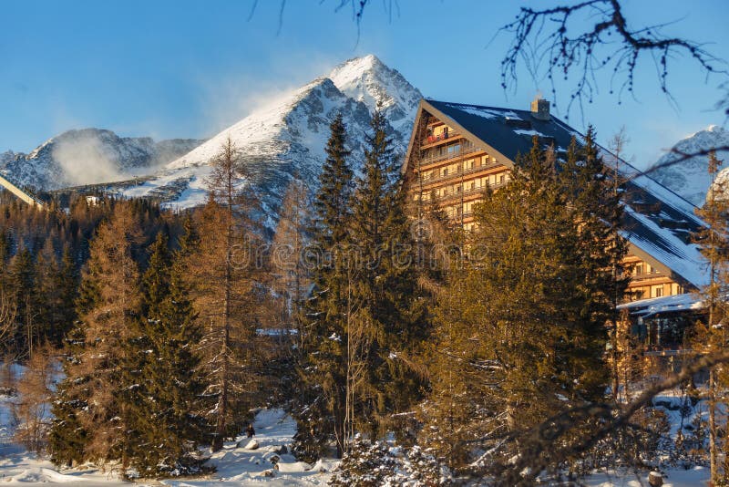 Winter view of the Strbske pleso village with hotel, coniferous forest and snowy peaks.