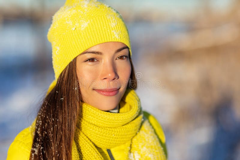 Winter woman Asian beauty girl walking in snow outside with yellow beanie knit hat and scarf for cold frost protection.