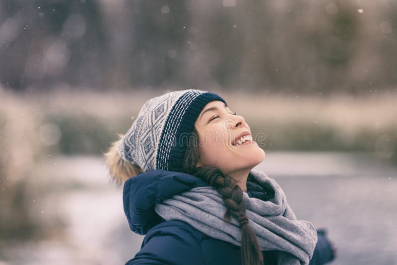 Winter woman happy enjoying snow falling on face outdoor forest nature Asian girl looking up wearing hat and scarf cold