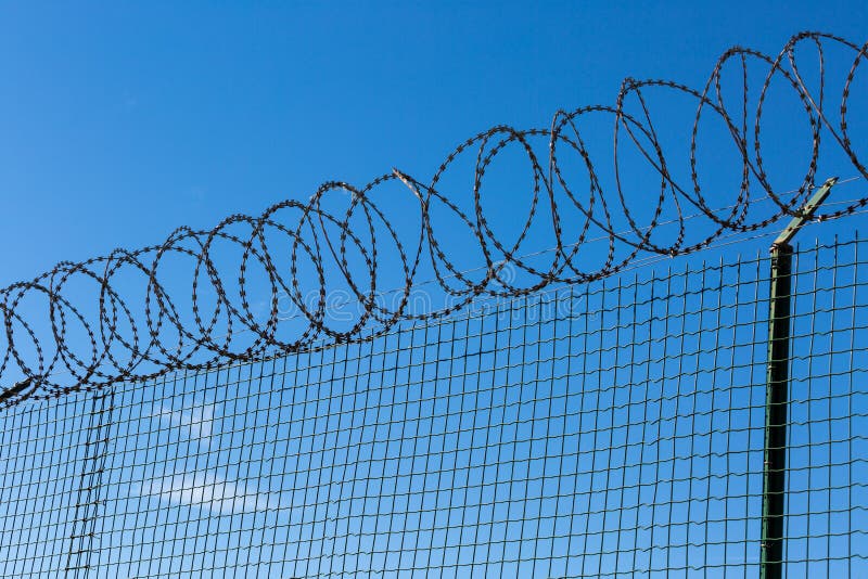 Wired Fence with Spiral Barbwire on Blue Sky Background