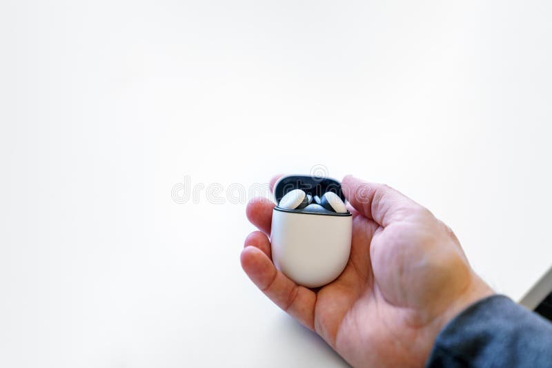 Wireless earbuds headphones in their charging case, held by a caucasian adult male hand. White desk and copy space.