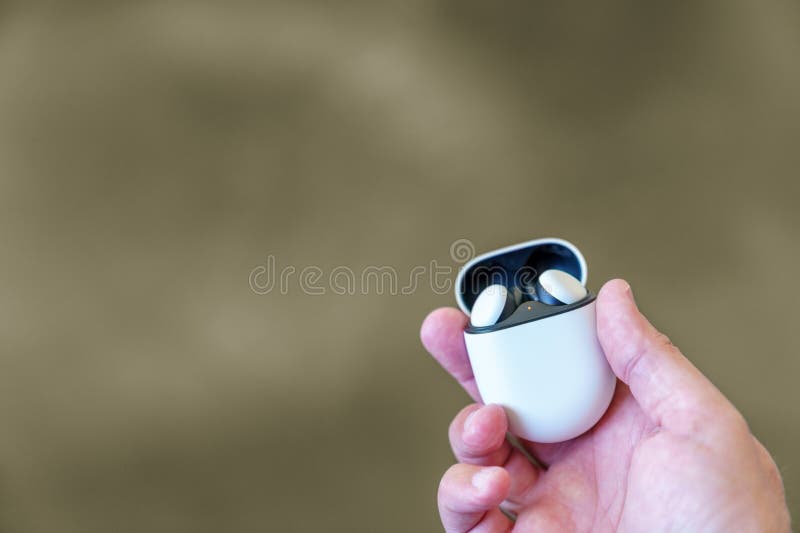 Wireless earbuds in their charging case, being held by a caucasian male hand. Blurred brown background and room for copy space.