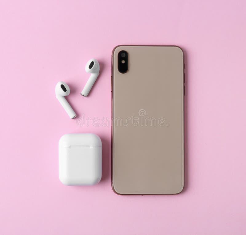 Earphones, mobile phone and charging case on pink background, flat lay