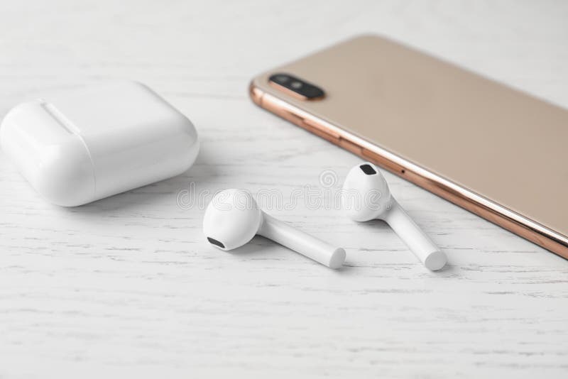 Wireless earphones, mobile phone and charging case on wooden table