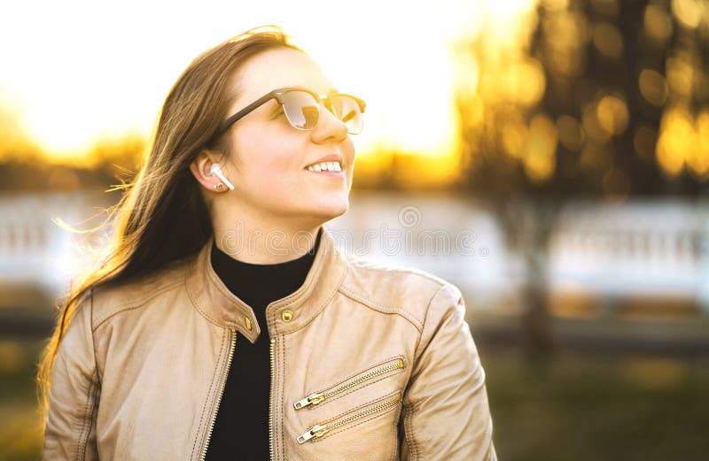 Wireless headphones, earbuds. Woman listening to music with earpods in a park. Happy young lady smiling.