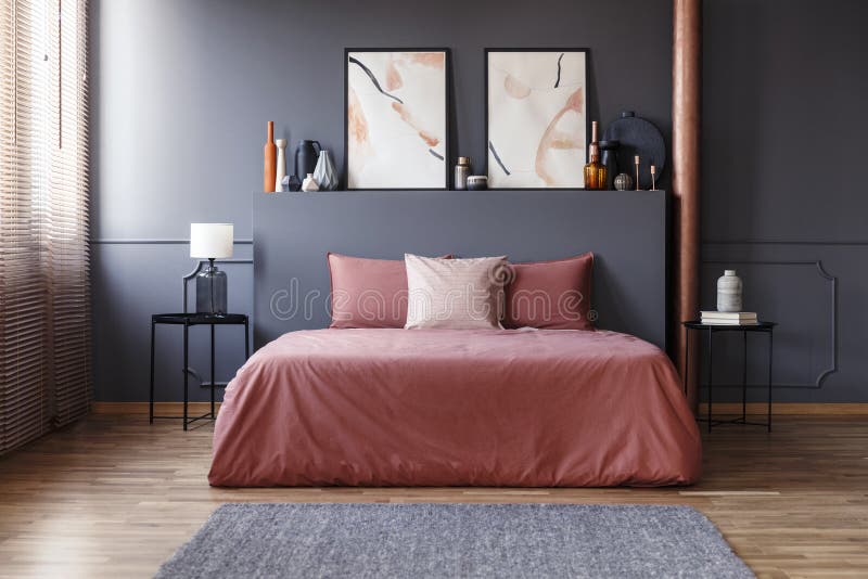 Real photo of a simple bedroom interior with dirty pink bedding on the bed standing against dark gray wall with molding, between two, metal bedside tables. Real photo of a simple bedroom interior with dirty pink bedding on the bed standing against dark gray wall with molding, between two, metal bedside tables