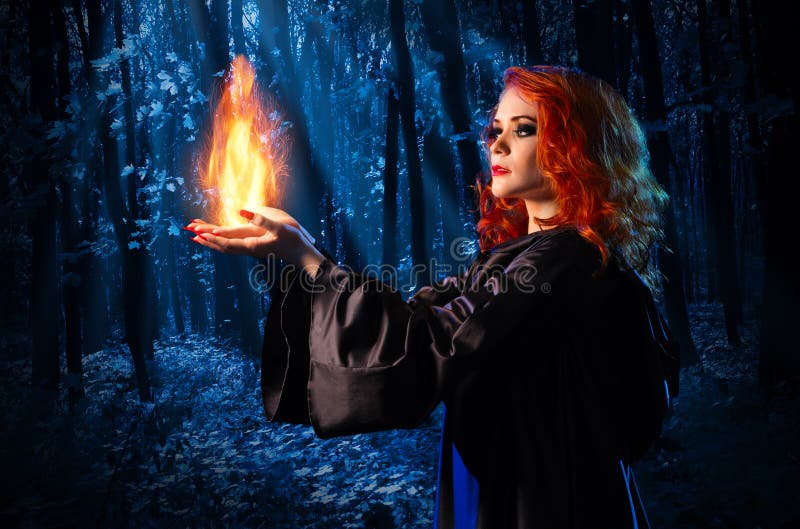 Witch in the night forest holds fire