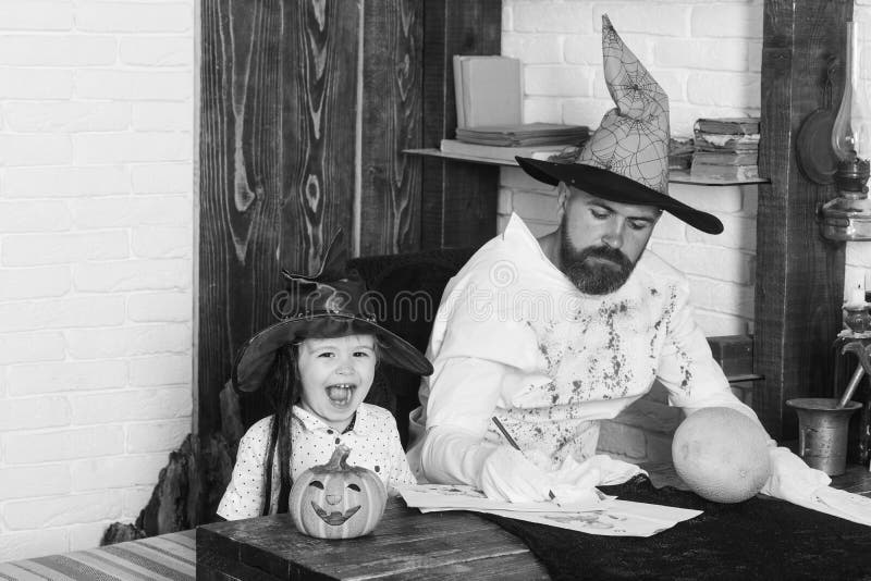 Witcher and little magician make decor for Halloween. Man and boy on wood and white brick background. Guy and kid with serious and happy faces in hats play stock photography Witcher and little magician make decor for Halloween. Man and boy on wood and white brick background. Guy and kid with serious and happy faces in hats play stock photography