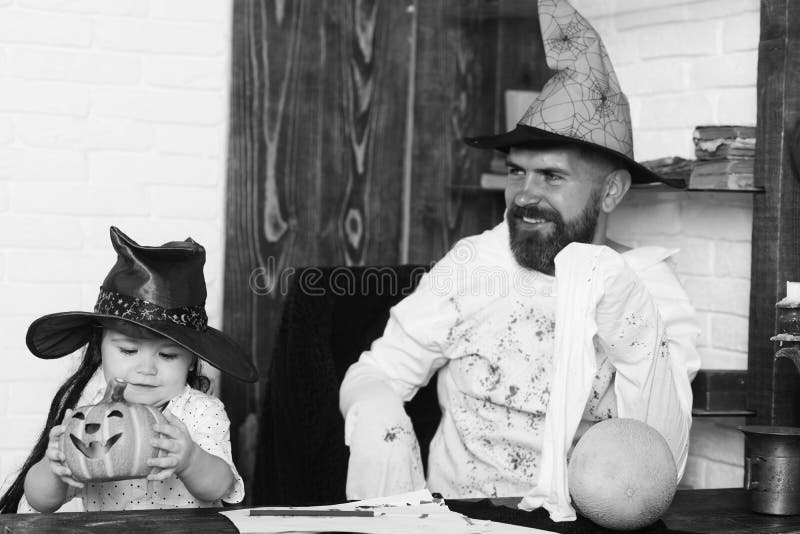 Witcher and little magician make Halloween decor. Man and boy on wooden and white brick wall background. Man and kid with happy faces in hats play with royalty free stock image Witcher and little magician make Halloween decor. Man and boy on wooden and white brick wall background. Man and kid with happy faces in hats play with royalty free stock image