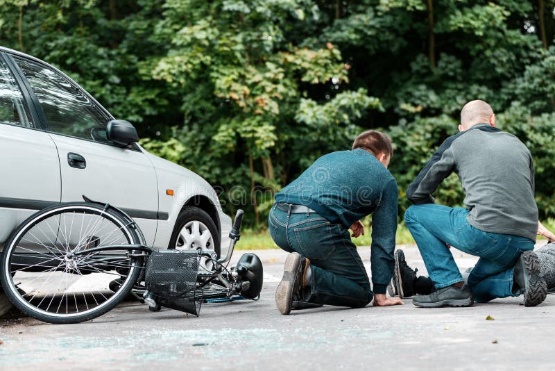 Witnesses of a road collision between a car and a bicycle helping a victim. Witnesses of a road collision between a car and a bicycle helping a victim