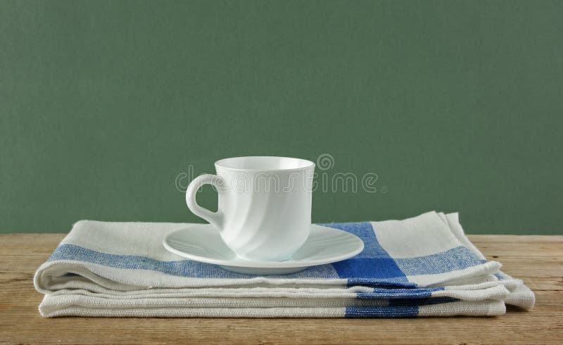 Witte koffiekop en theedoek op oude houten lijst over groene bedelaars royalty-vrije stock foto Witte koffiekop en theedoek op oude houten lijst over groene bedelaars royalty-vrije stock foto