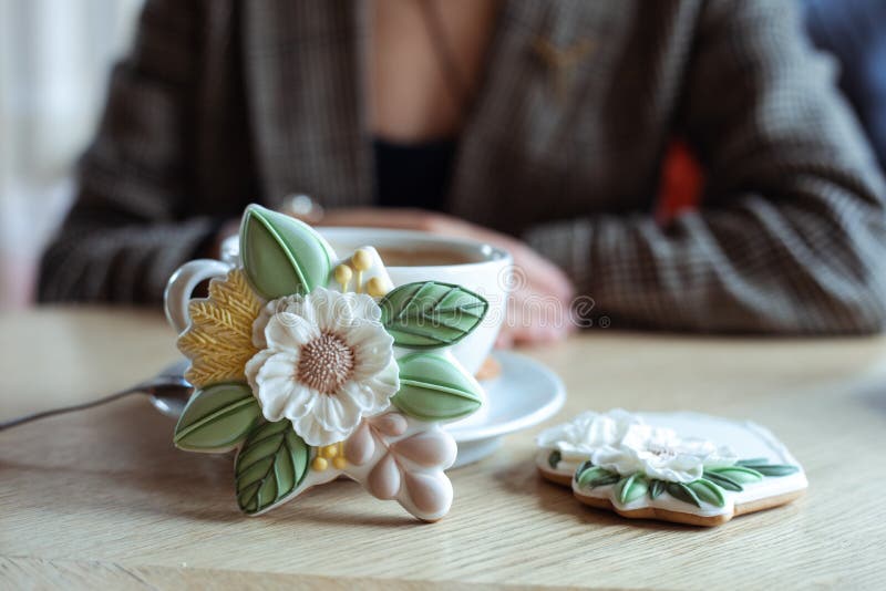 Witte kop koffie op de schotel en mooie koekjes in de vorm van een ijsbloem op tafel op de voorgrond , silhouette van de dame op d