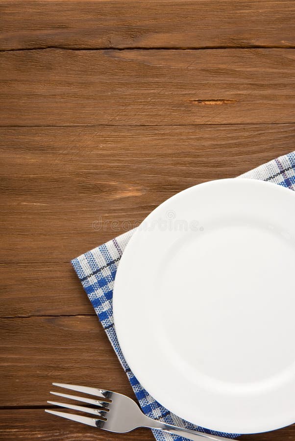 White plate and fork at napkin on wooden background. White plate and fork at napkin on wooden background