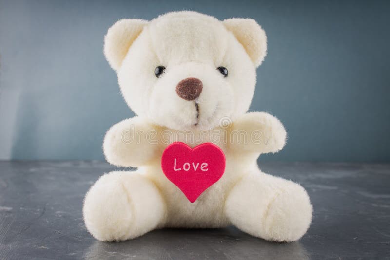 Witte stuk speelgoed teddybeer met hart op een grijze achtergrond Het symbool stock fotografie Witte stuk speelgoed teddybeer met hart op een grijze achtergrond Het symbool stock fotografie